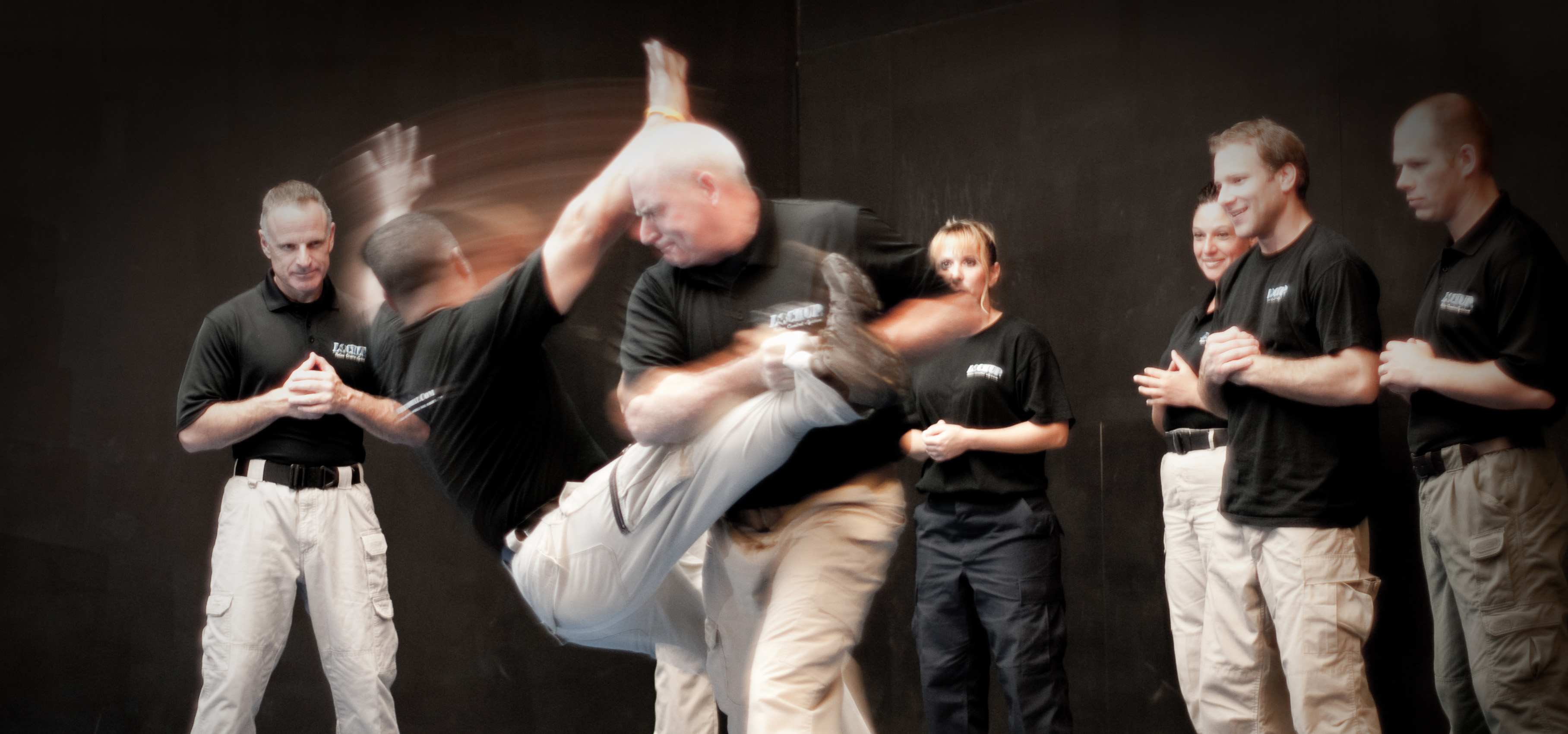 An instructor and a student practicing a grappling or self-defense maneuver on a training mat during a combat training session.