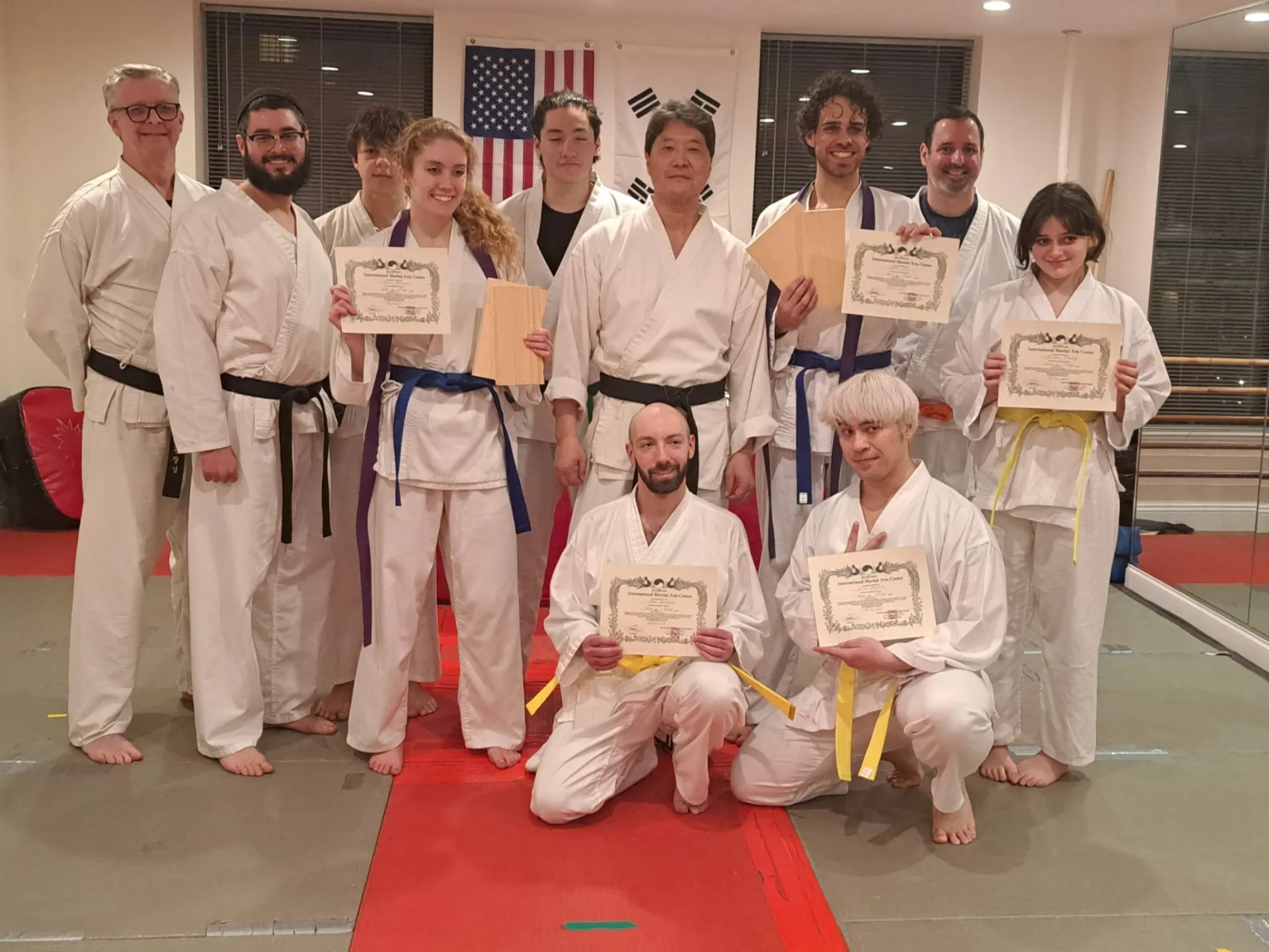 Adult students holding promotion certificates with instructors at International Martial Arts Center in New York City