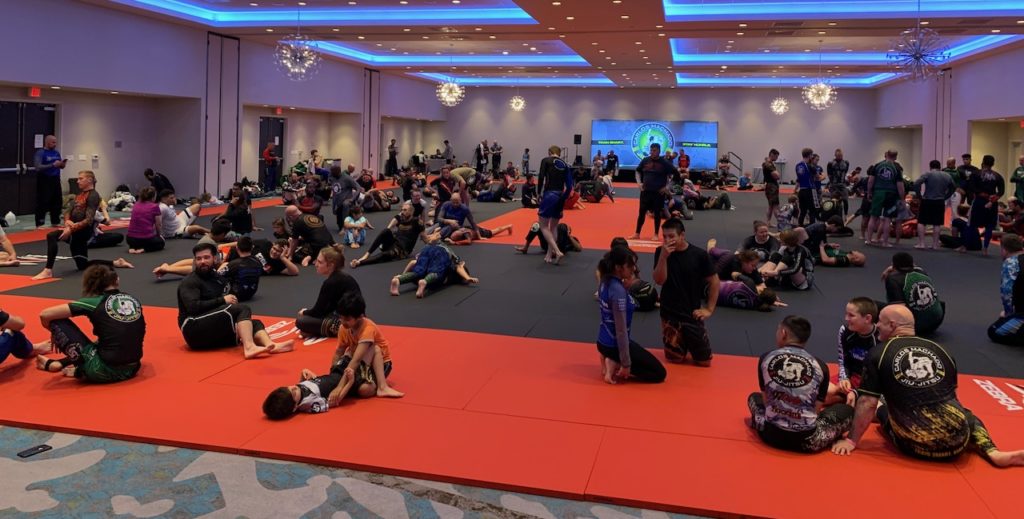 Large group of martial artists training on mats at an event